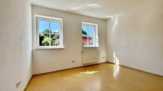 Sonniger Raum mit hellem Boden und zwei Fenstern, die viel Licht spenden.