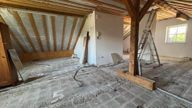 Geräumiger Dachboden mit Holzbalken und Fenster, ideal für zukünftige Wohnräume.