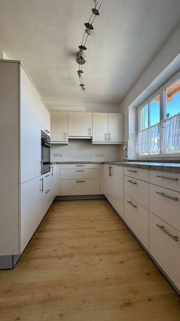 Moderne Küche mit hellen Schränken, Einbaugeräten und Holzoptik-Boden.