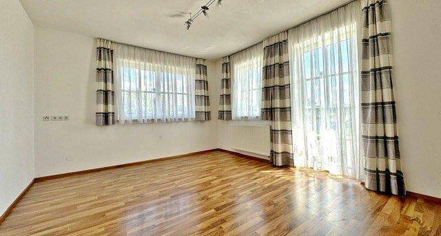 Heller Wohnraum mit Holzoptik-Boden, großen Fenstern und Zugang zu einem Balkon.