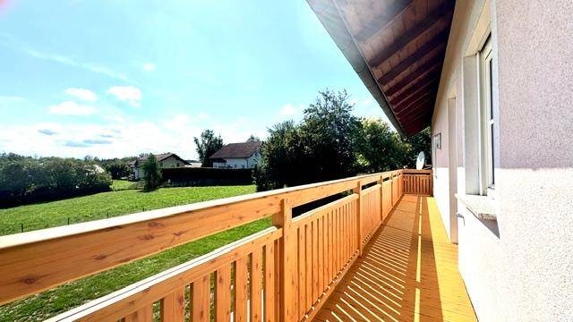 Langer Holzbalkon mit Blick auf die grüne Umgebung und viel Sonnenlicht.