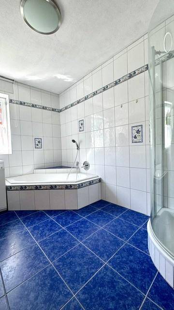 Badezimmer mit blauen Bodenfliesen, Eckbadewanne und separater Duschkabine.