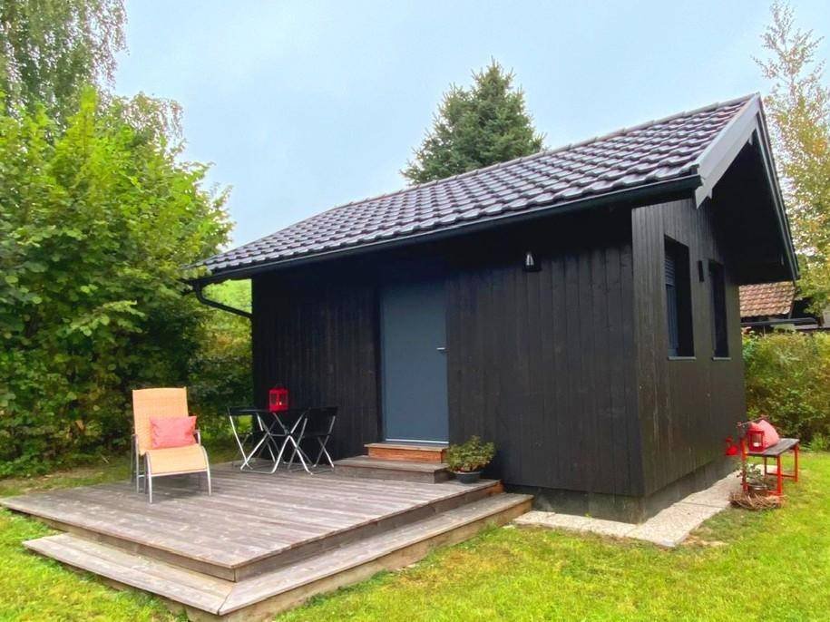 Kleines schwarzes Holzhaus mit Holzterrasse und grünem Gartenbereich.