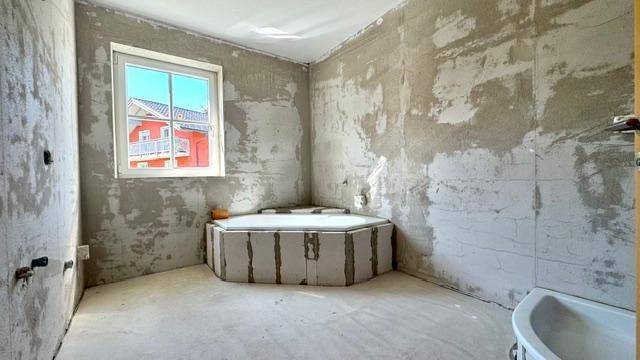 Badezimmer im Rohbau mit vorbereiteter Eckbadewanne und Fenster.