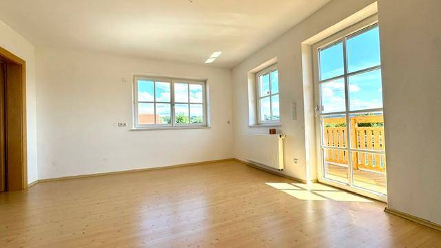Geräumiger Wohnraum mit hellem Boden, großen Fenstern und Zugang zum Balkon.
