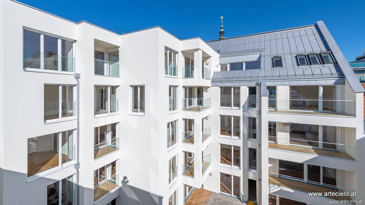 Nahaufnahme der modernen weißen Fassade mit zahlreichen Balkonen und großen Fensterflächen.