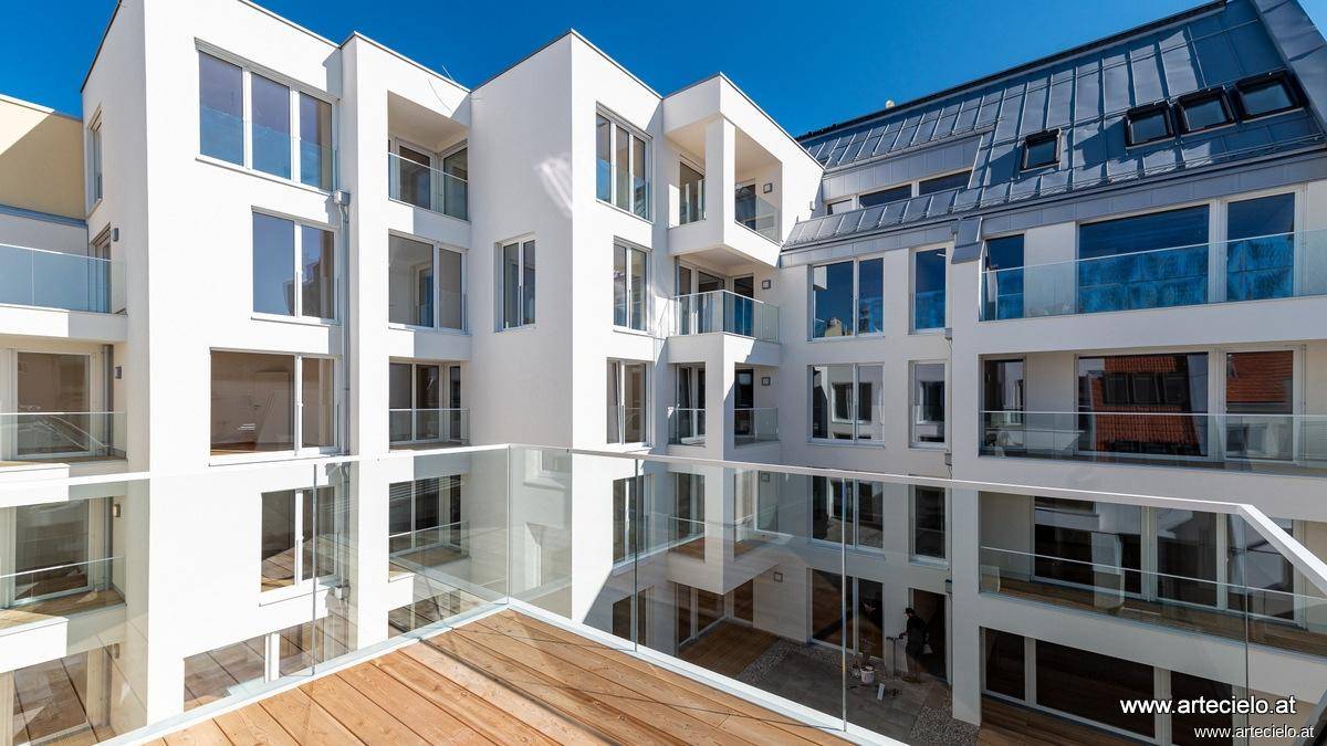 Moderner Innenhof mit hellen Fassaden, Glasbalkonen und einer Holzterrasse im Vordergrund.