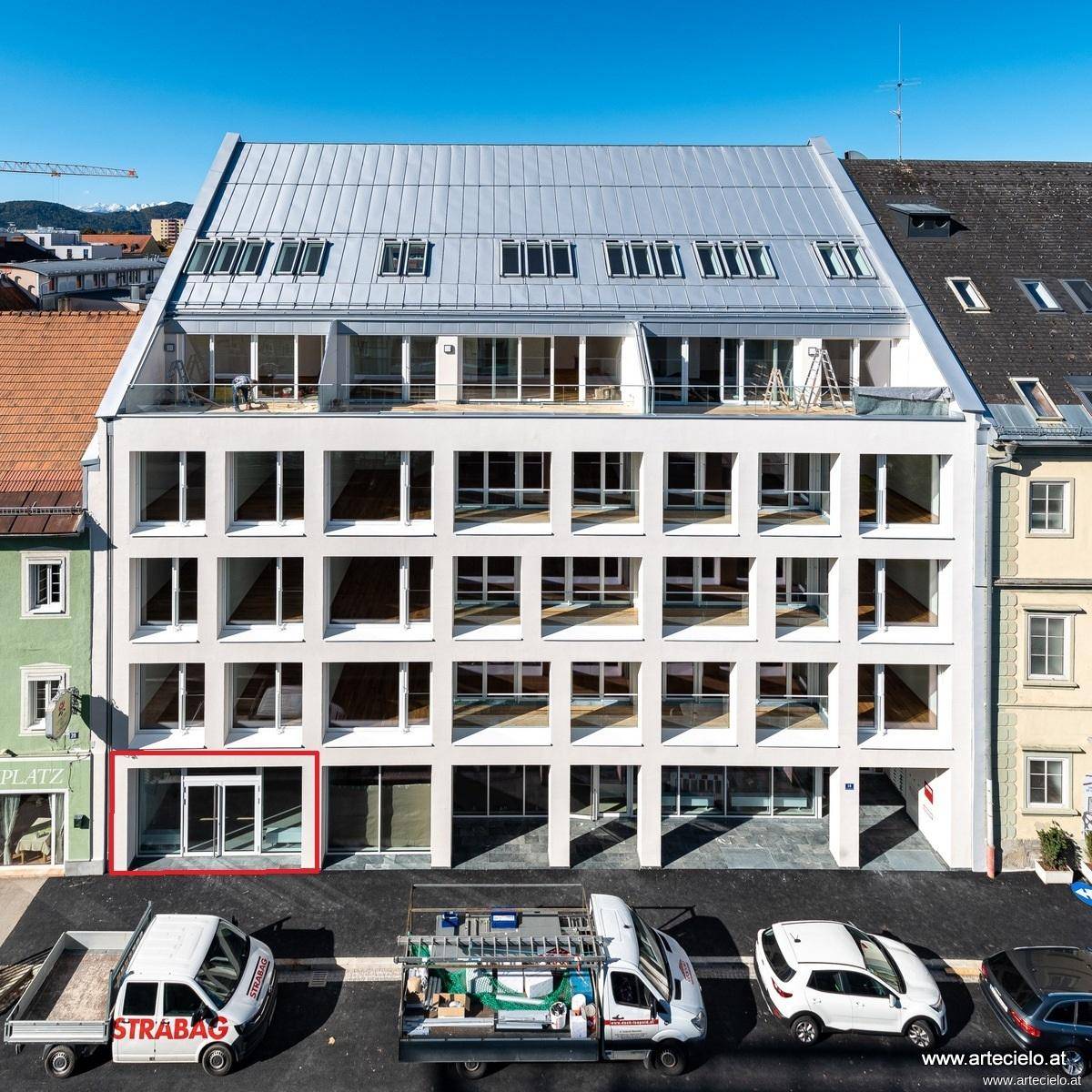 Moderne Gebäudefassade mit großen Fenstern, Balkonen und einem Satteldach in städtischer Umgebung.