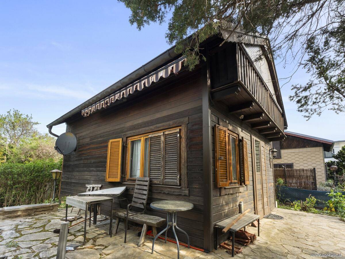 Rustikales Holzhaus mit kleiner gepflasterter Terrasse und Gartenmöbeln im Freien.