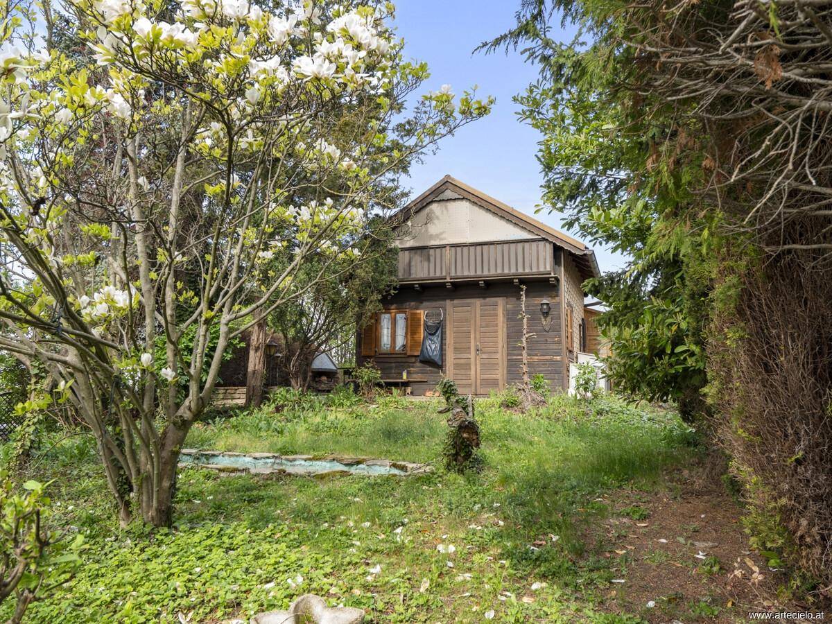 Idyllischer Gartenbereich mit blühendem Baum und einem charmanten Holzhaus im Hintergrund.