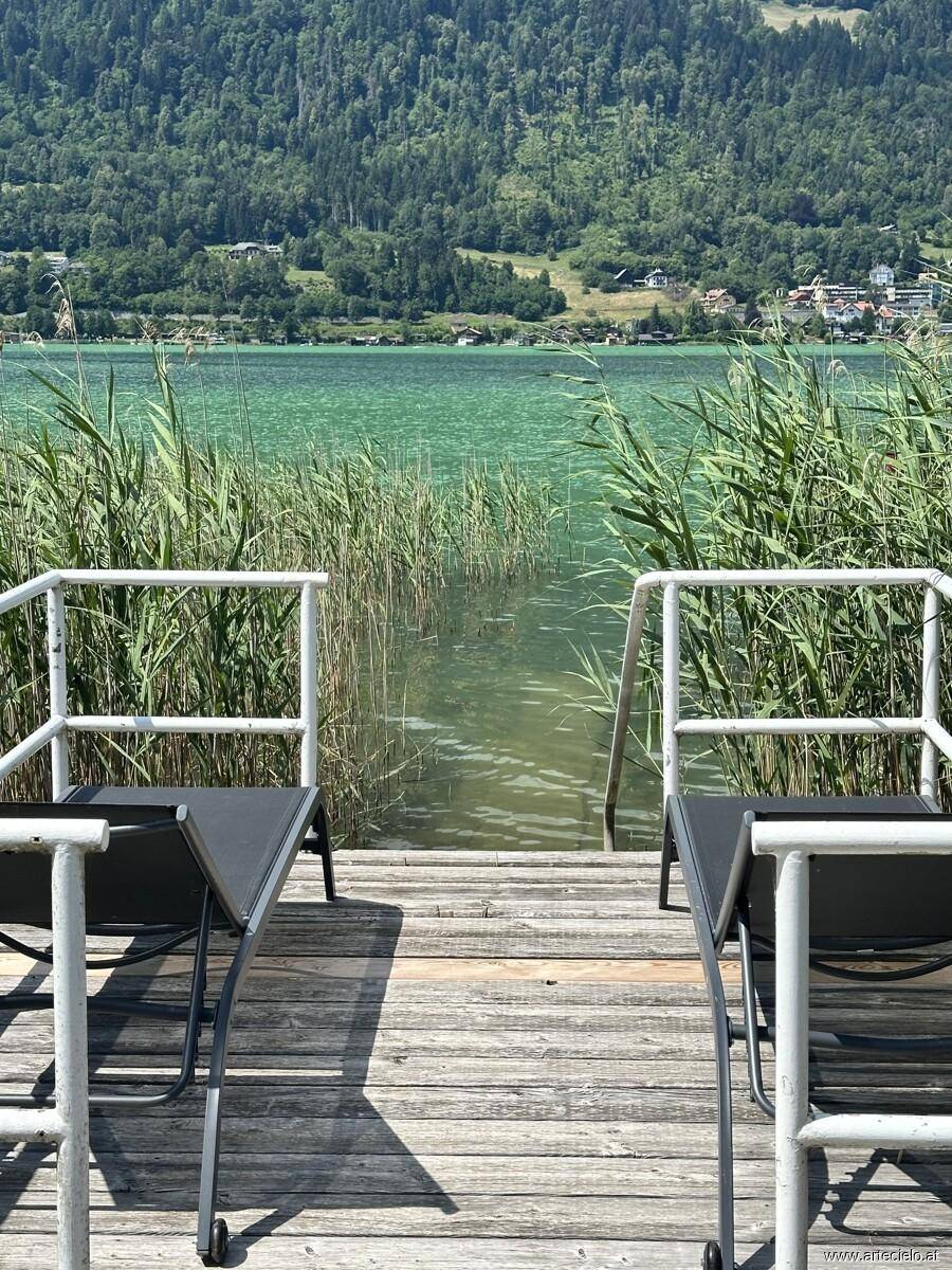 Zwei Liegestühle auf einem Holzsteg bieten einen direkten Blick auf das klare Seewasser und die Berge.
