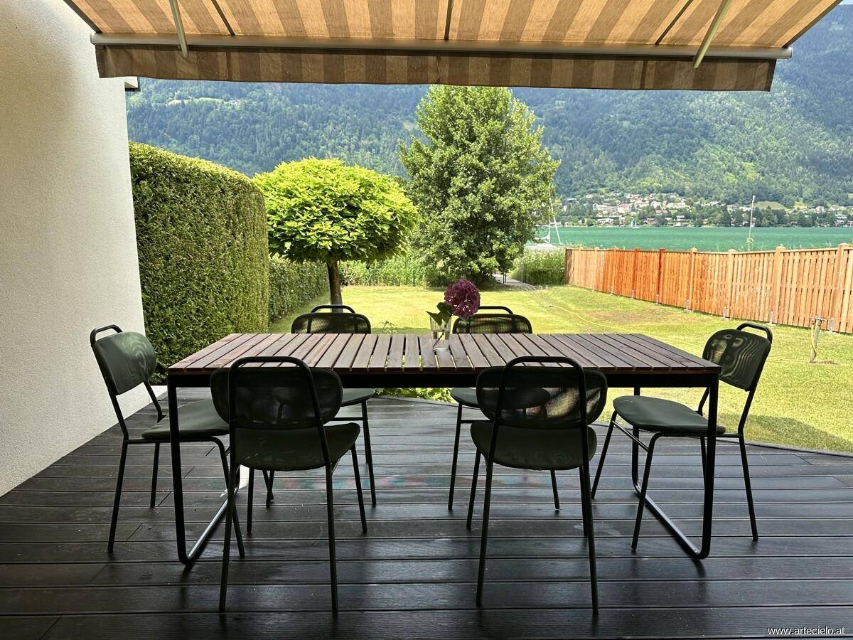 Gemütlicher Essbereich auf der Terrasse unter einer Markise mit weitem Blick auf den See und die Berge.