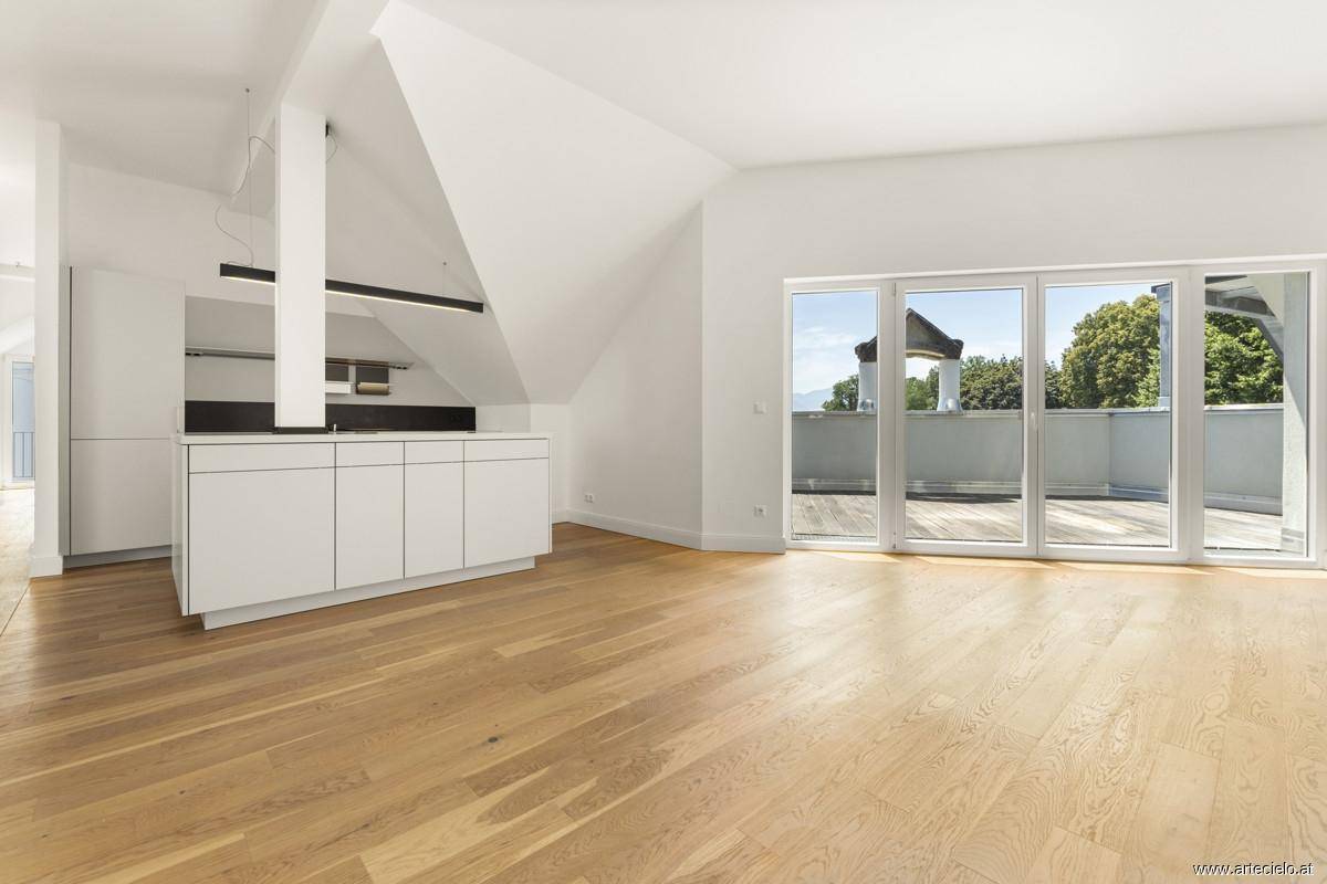 Heller offener Küchenbereich mit Holzboden, Dachschrägen und Zugang zu einer großen Terrasse.