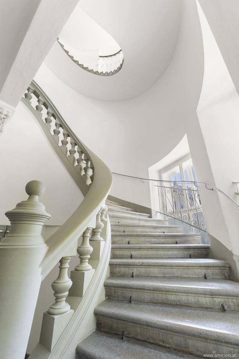 Elegantes Treppenhaus mit geschwungener Balustrade, Steinstufen und viel natürlichem Licht.