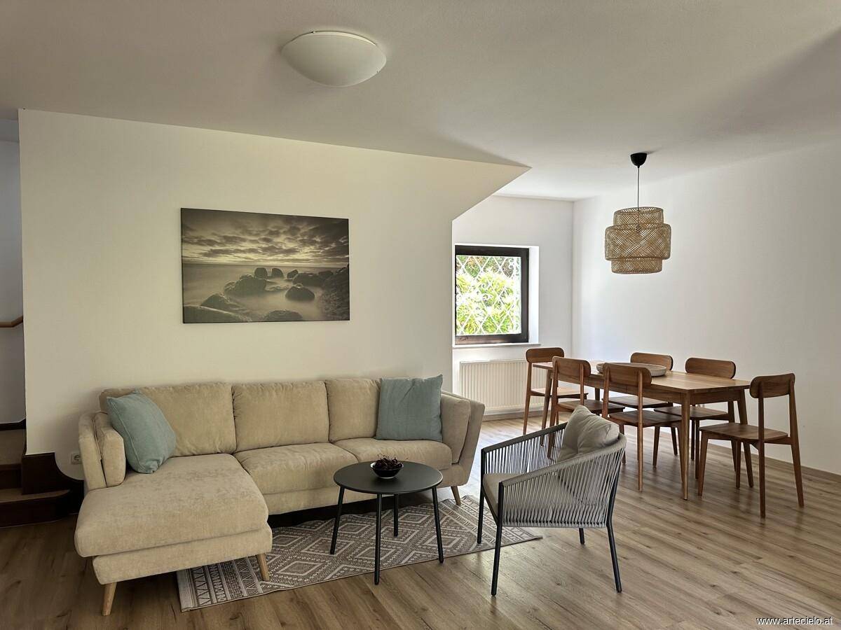 Heller Wohn- und Essbereich mit beigem Ecksofa, Holzboden und modernem Esstisch.