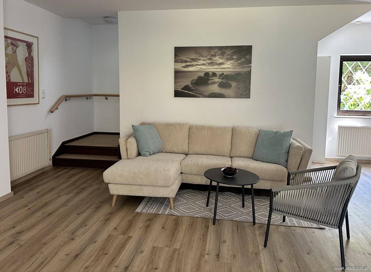 Gemütlicher Wohnbereich mit beigem Ecksofa, Holzboden und Zugang zur Treppe.