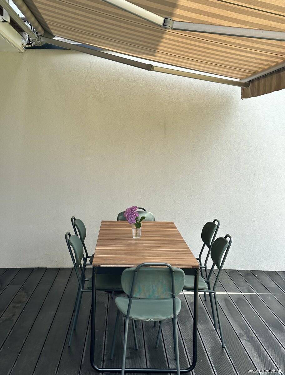 Überdachte Terrasse mit Holztisch und Stühlen, ideal für Mahlzeiten im Freien.