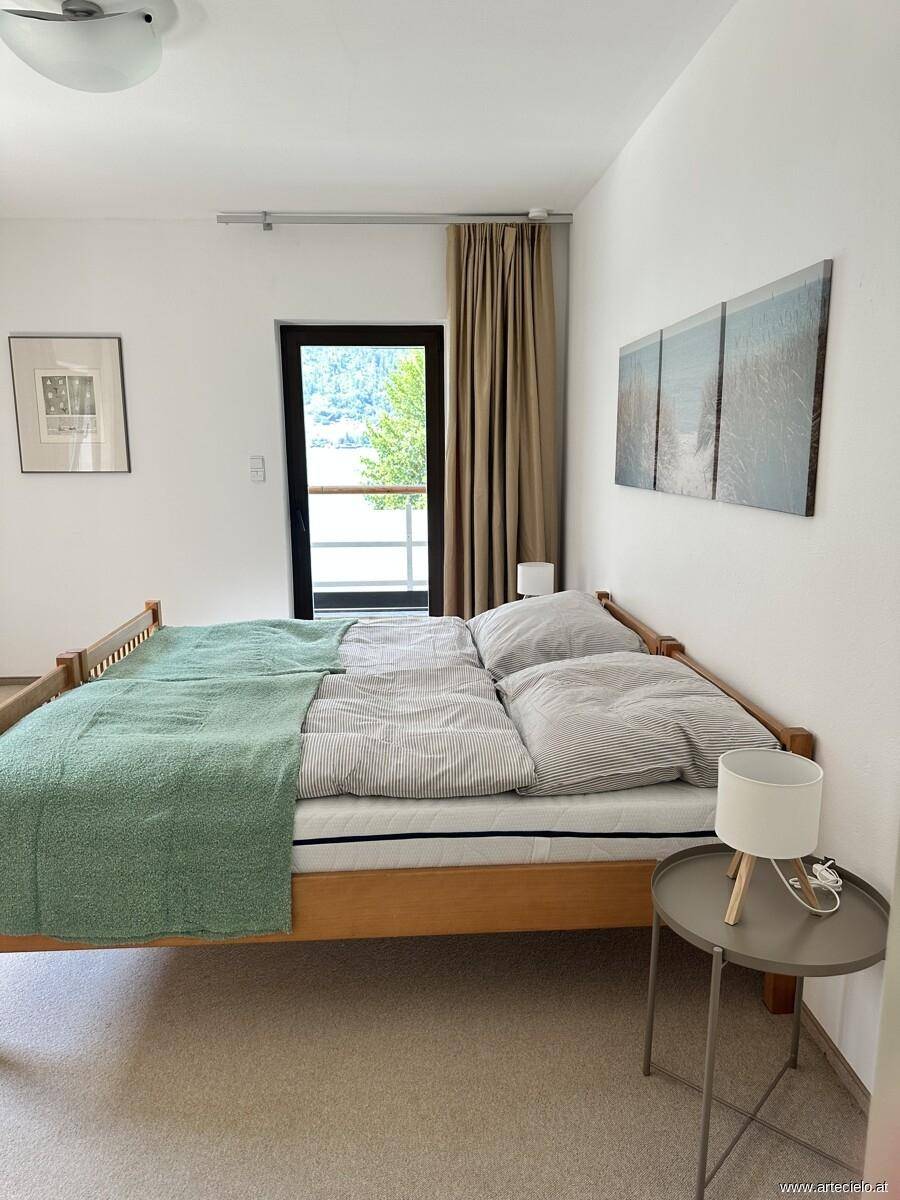 Schlafzimmer mit Doppelbett und Blick auf den See durch die Balkontür.