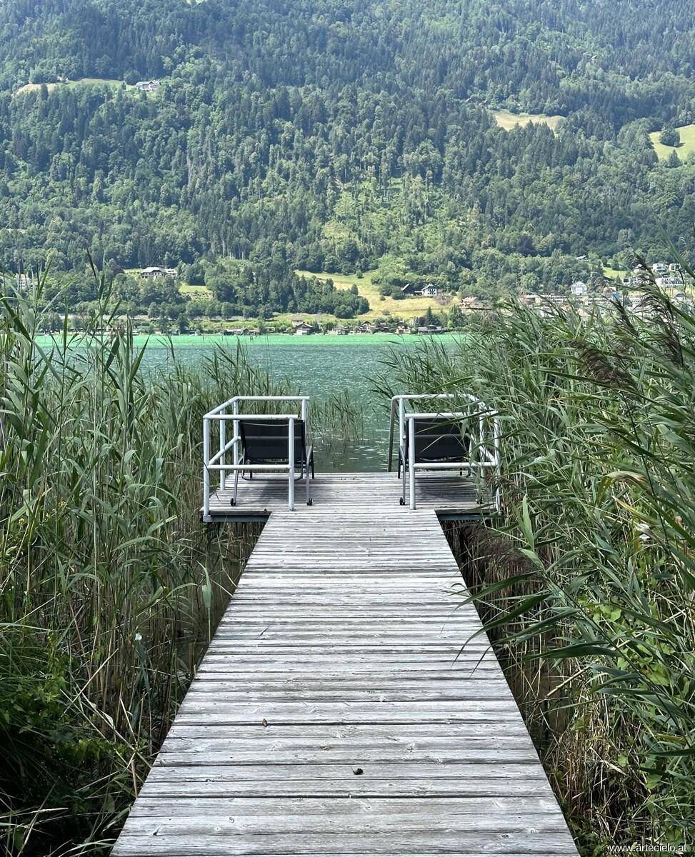 Holzsteg führt zu einem malerischen See mit bewaldeten Bergen im Hintergrund.
