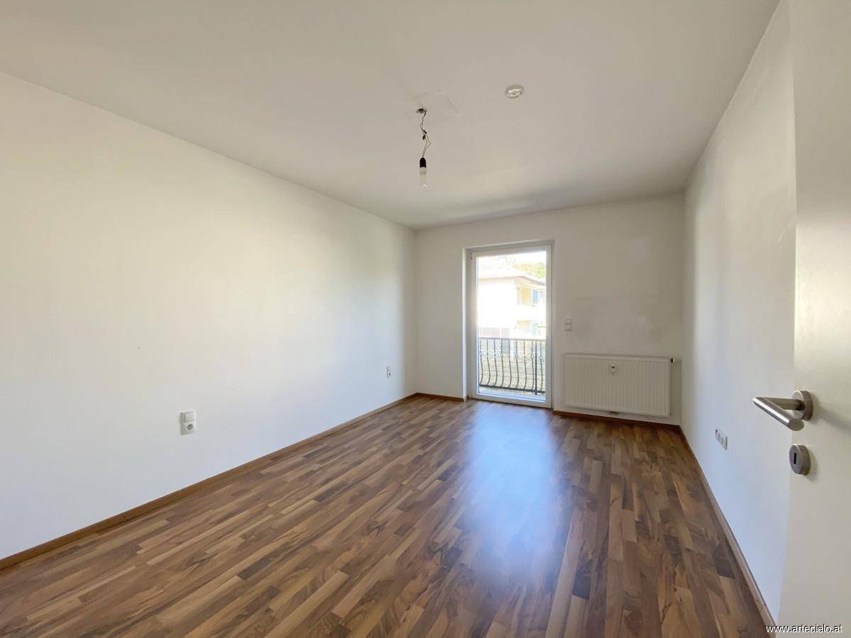 Leeres Zimmer mit Laminatboden und weiß gestrichenen Wänden, mit Zugang zu einem französischen Balkon.
