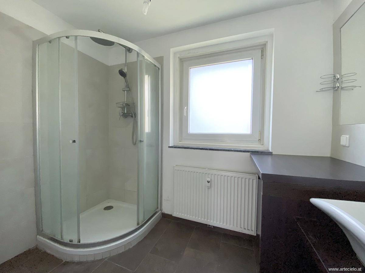 Badezimmer mit moderner Duschkabine, Fenster und dunklem Waschtischbereich, hell und funktional.
