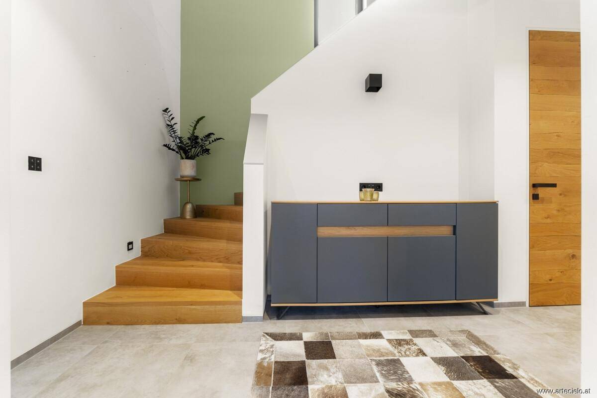 Treppenbereich mit Holzstufen, moderner Kommode und grün akzentuierter Wand.