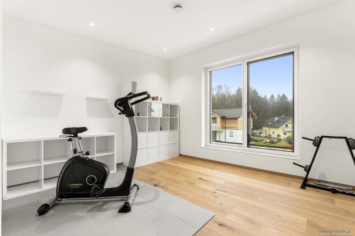 Heller Fitnessraum mit Fenster, Holzboden und Blick ins Grüne.