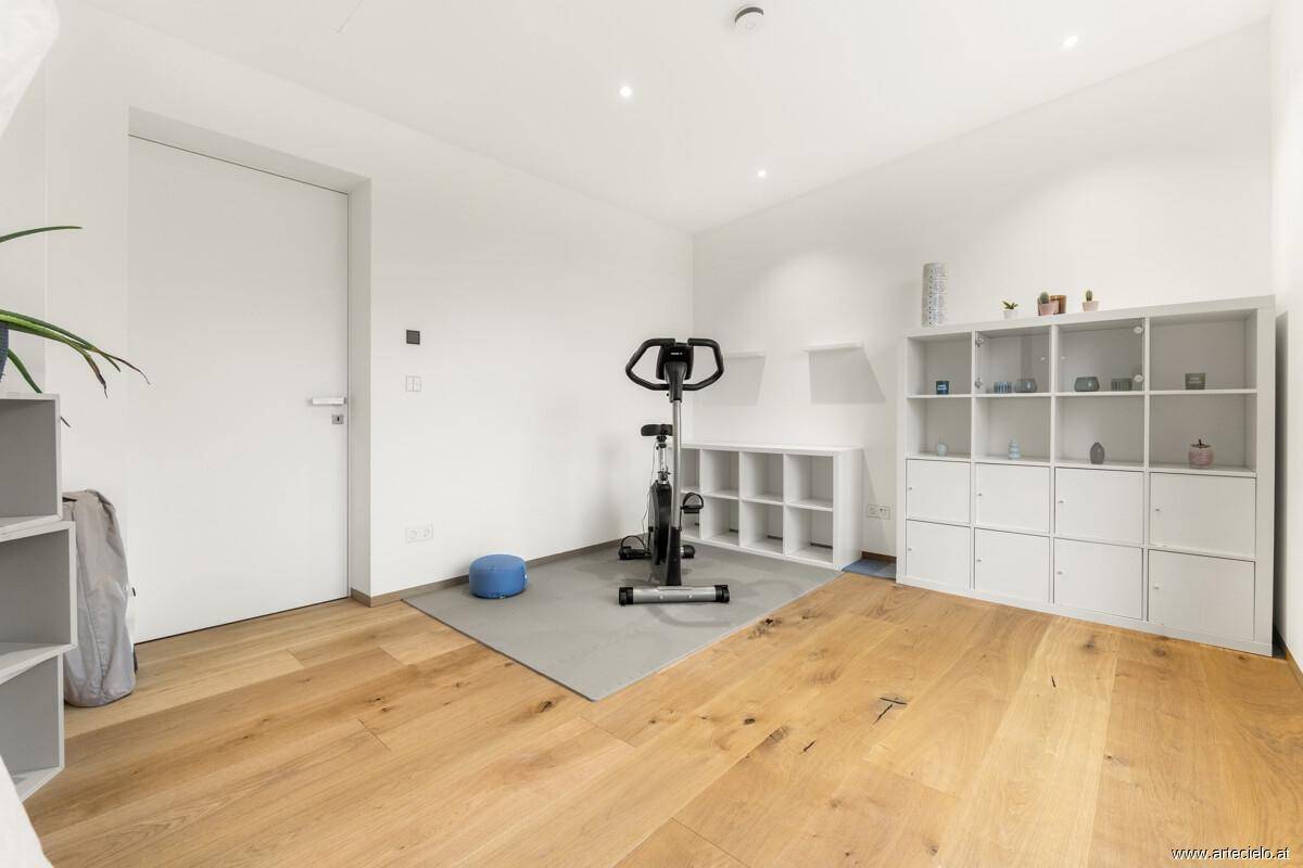Fitnessraum mit Holzboden, Regalen und Trainingsgerät.