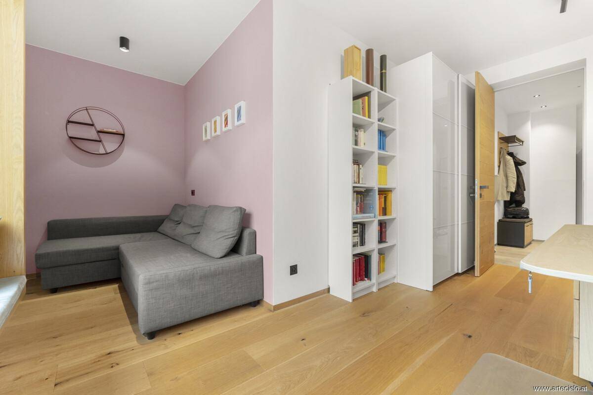 Gemütlicher Wohnbereich mit Sofa, Bücherregal und rosa Akzentwand.
