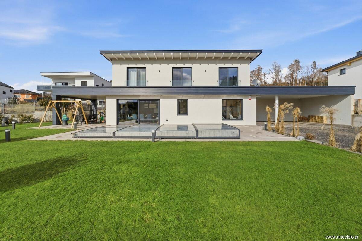 Rückansicht des modernen Hauses mit großem Rasen, Pool und Spielplatz.