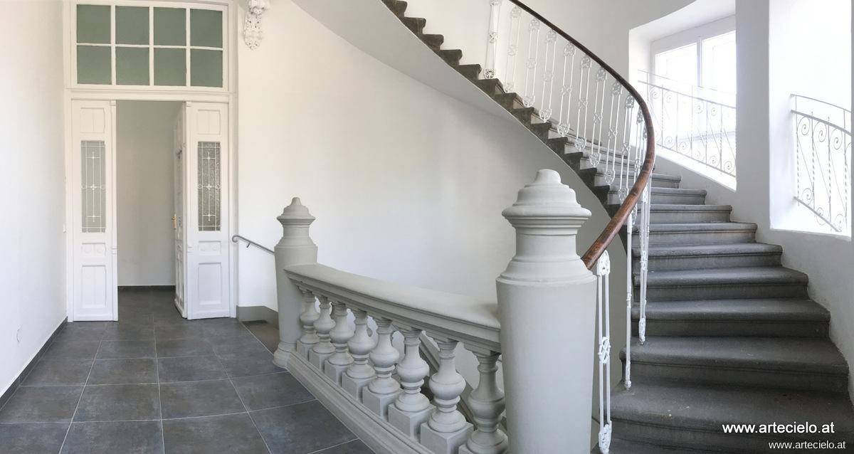 Elegantes Treppenhaus mit geschwungener Treppe, kunstvollem Geländer und hohen Decken.