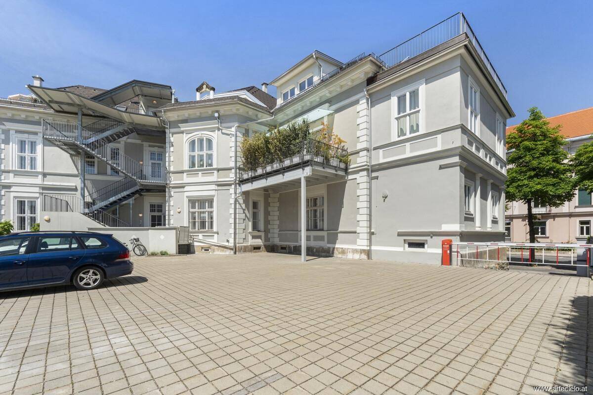 Rückseite des Gebäudes mit gepflastertem Hof, Außentreppe und kleinem Balkon.