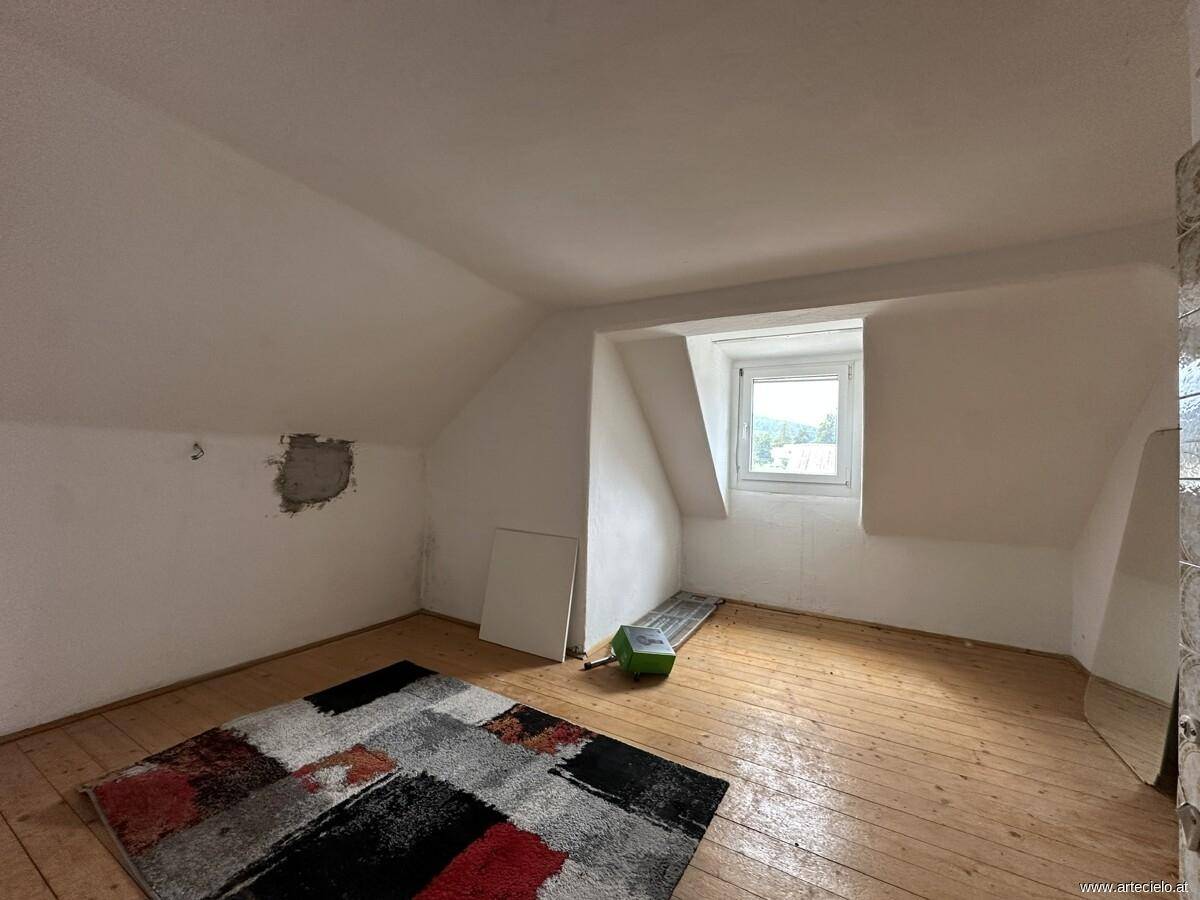 Dachgeschosszimmer mit schrägen Wänden, Holzboden und Fenster, das Renovierungsbedarf aufweist.