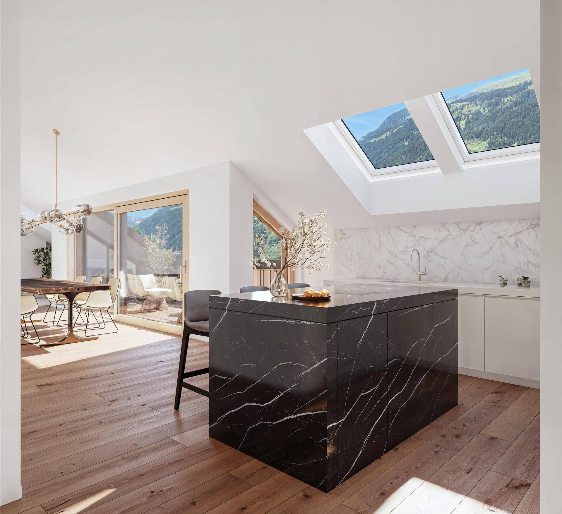 Moderne Küche mit schwarzer Marmorinsel, Dachfenstern und Bergblick, offen zum Essbereich und Balkon.