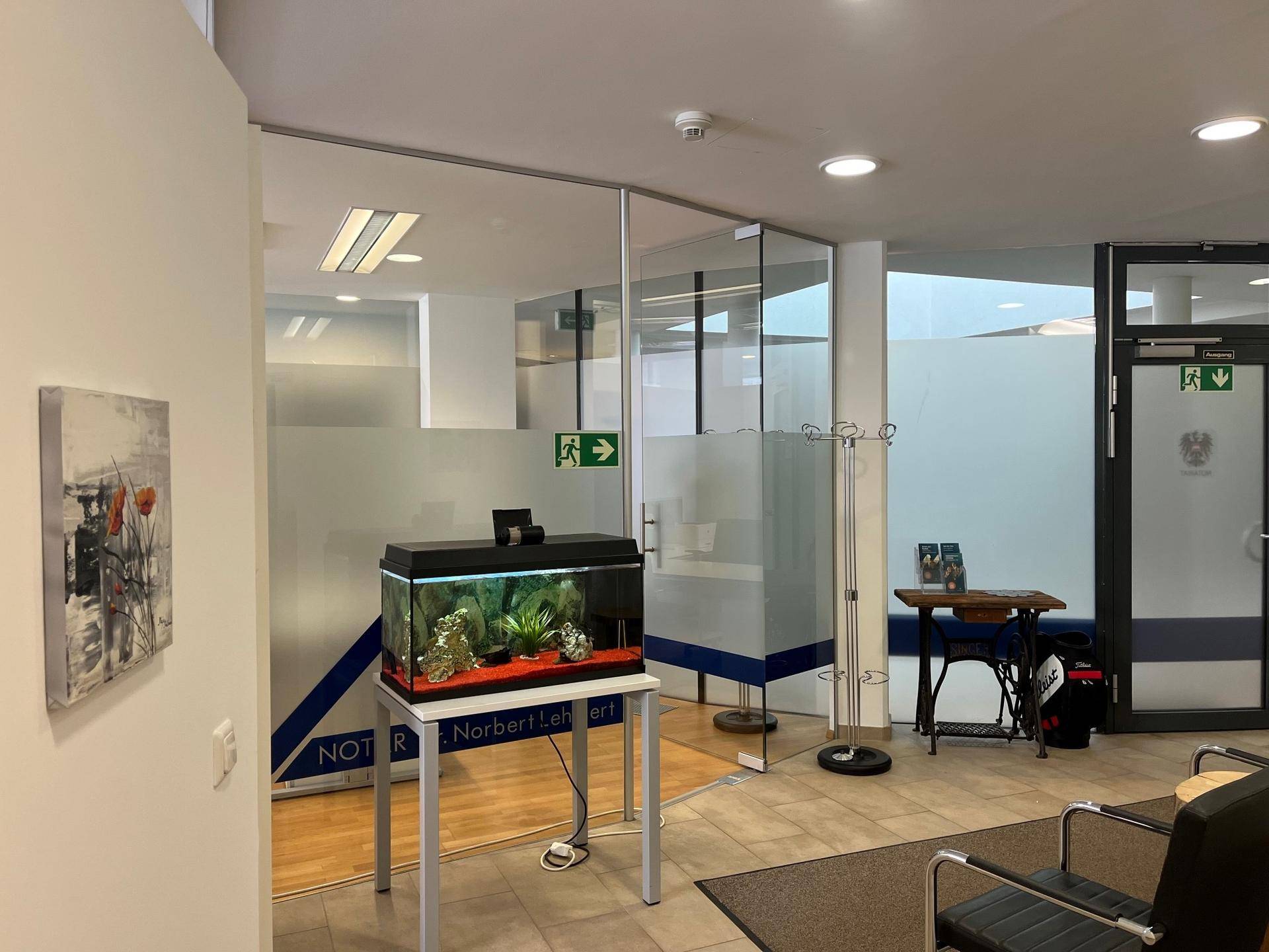Empfangsbereich mit Glaswänden, einem Aquarium und bequemen Sitzgelegenheiten, ausgestattet mit Fliesenboden.
