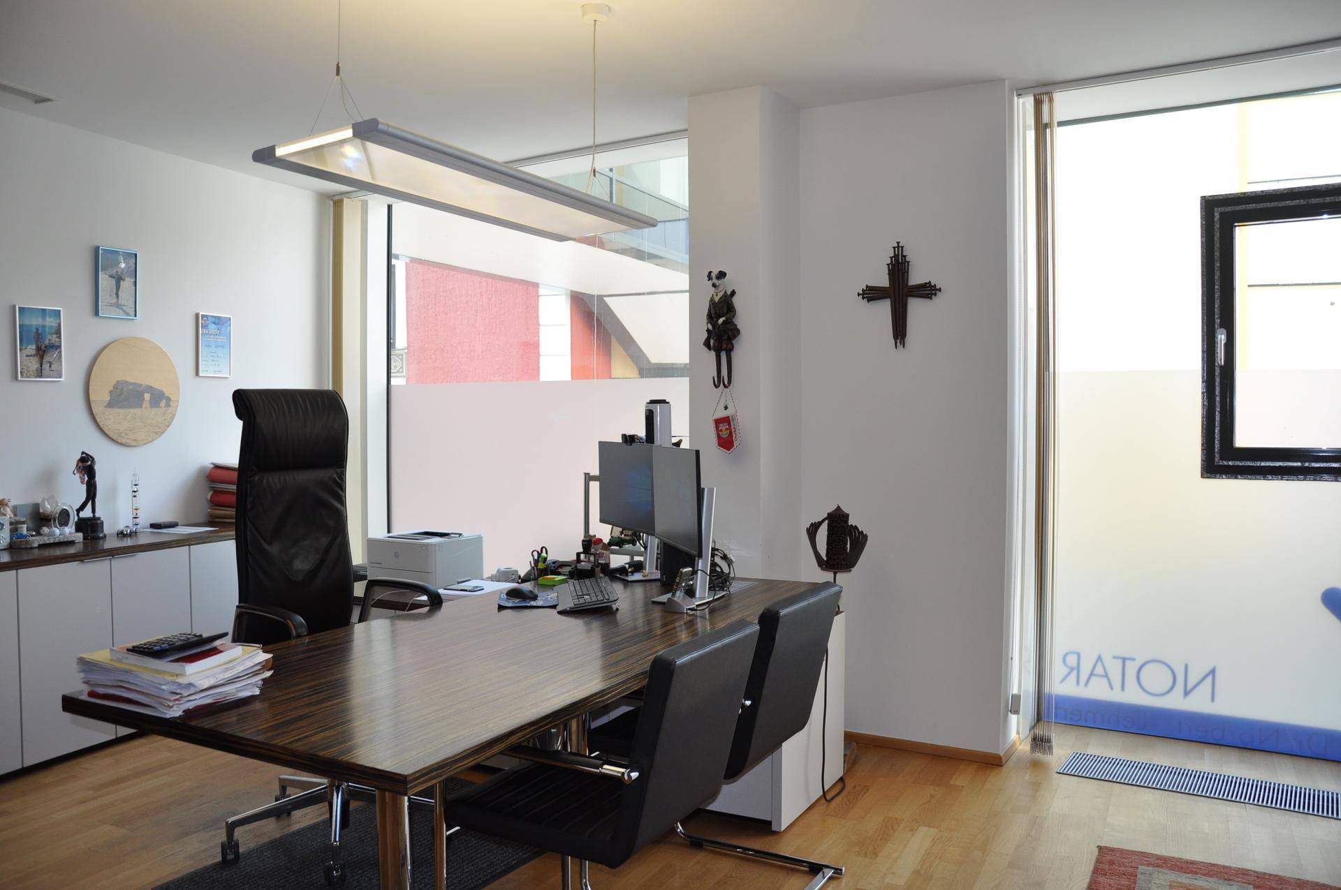 Geräumiges Büro mit Holzboden, modernem Schreibtisch und Bürostühlen, beleuchtet durch eine lange Deckenleuchte.