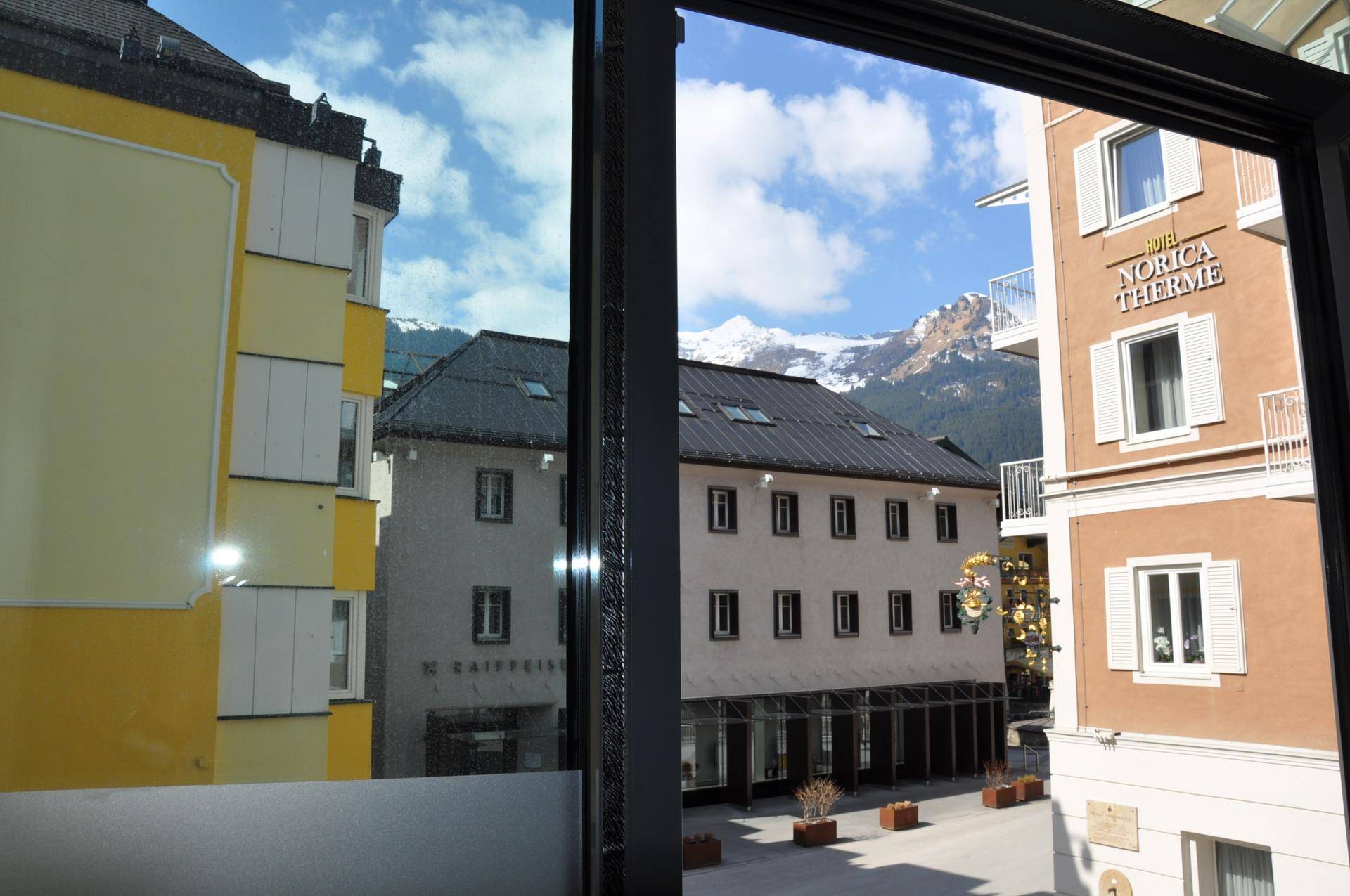 Blick aus einem Fenster auf eine belebte Straße mit Gebäuden und schneebedeckten Bergen im Hintergrund.
