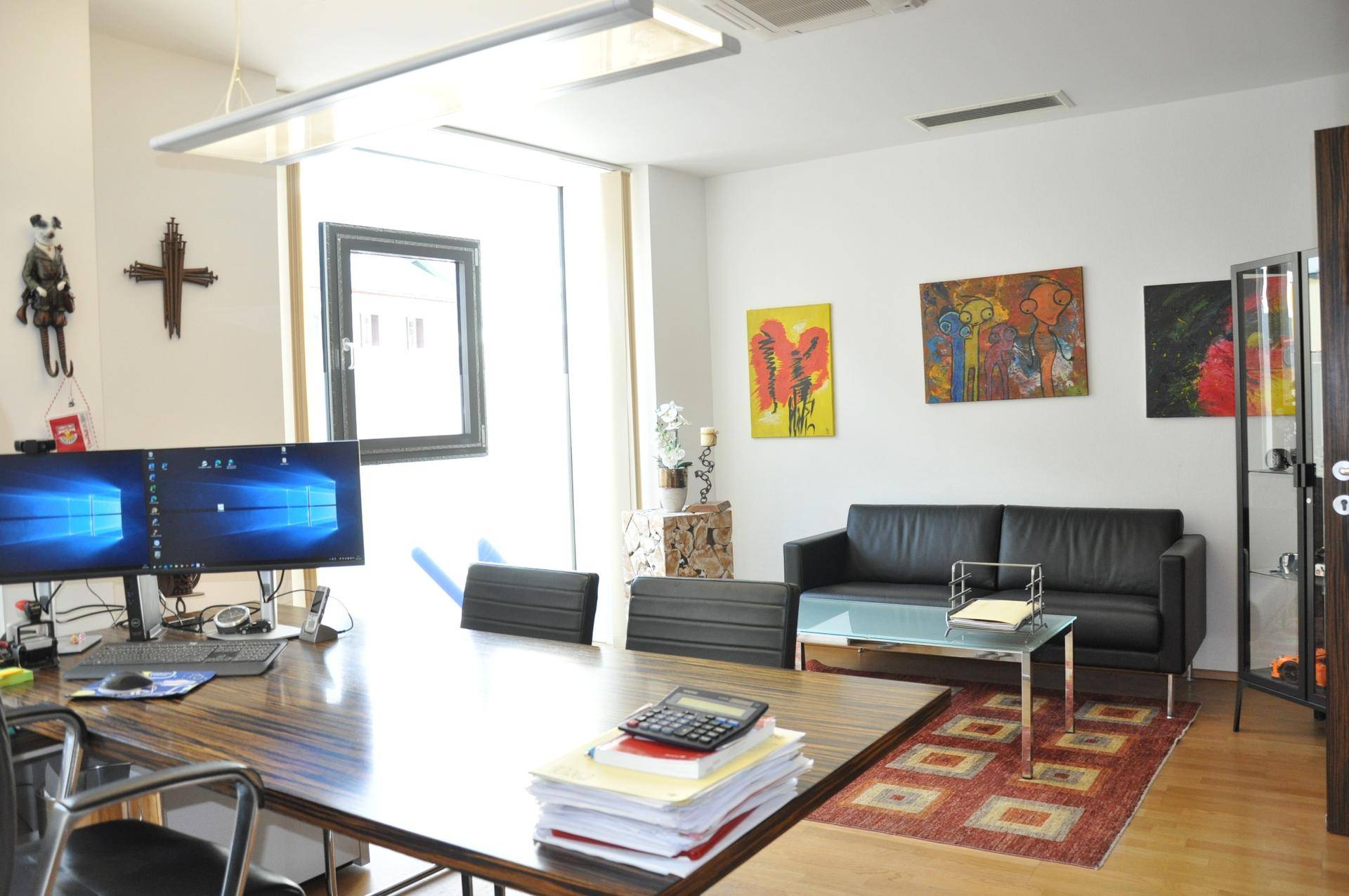 Helles Büro mit Sitzbereich, modernem Schreibtisch und Kunstwerken an den Wänden, ausgestattet mit Holzboden.