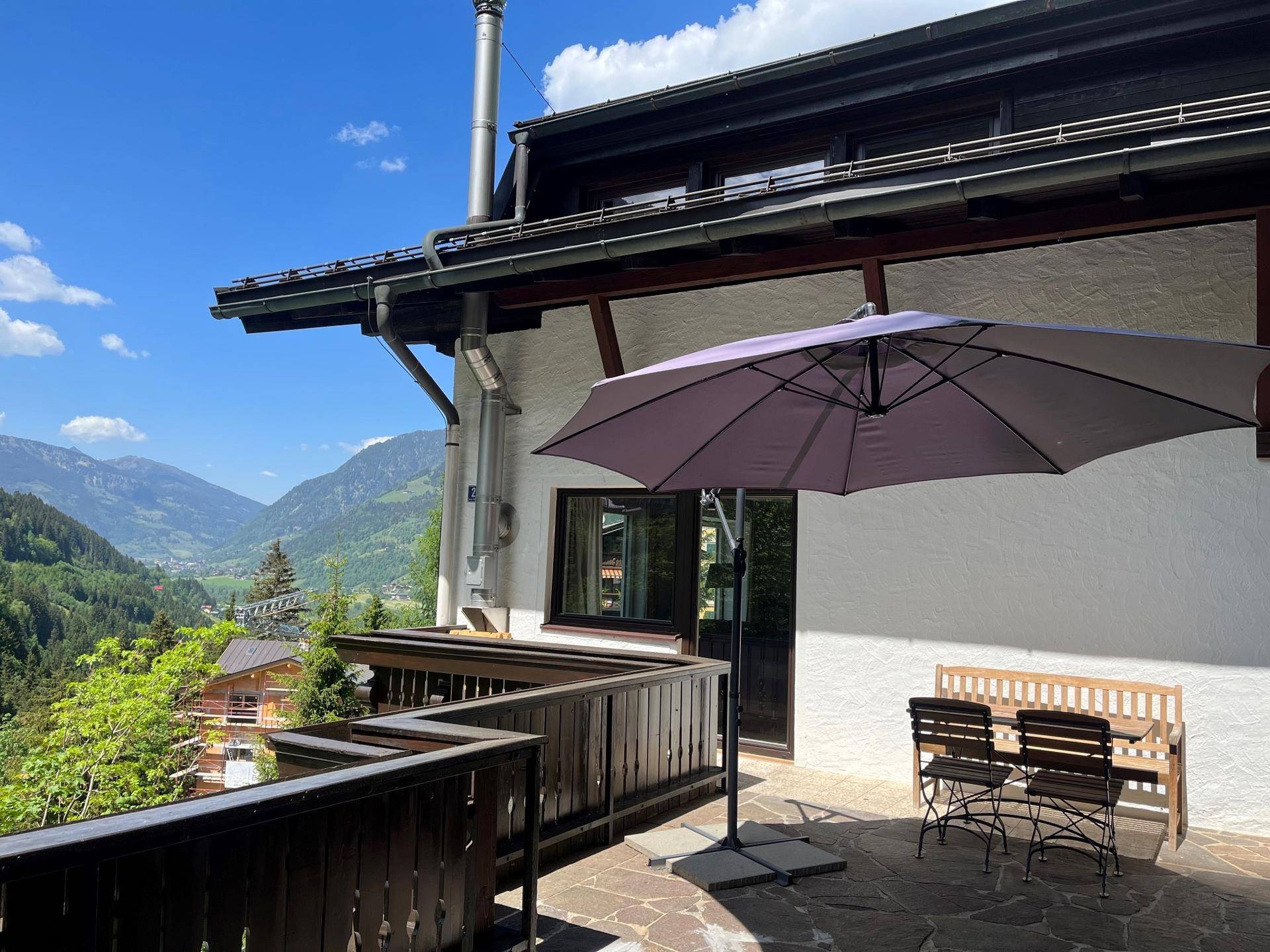 Sonniger Terrassenbereich mit Sitzgelegenheiten, Sonnenschirm und weitem Bergblick.
