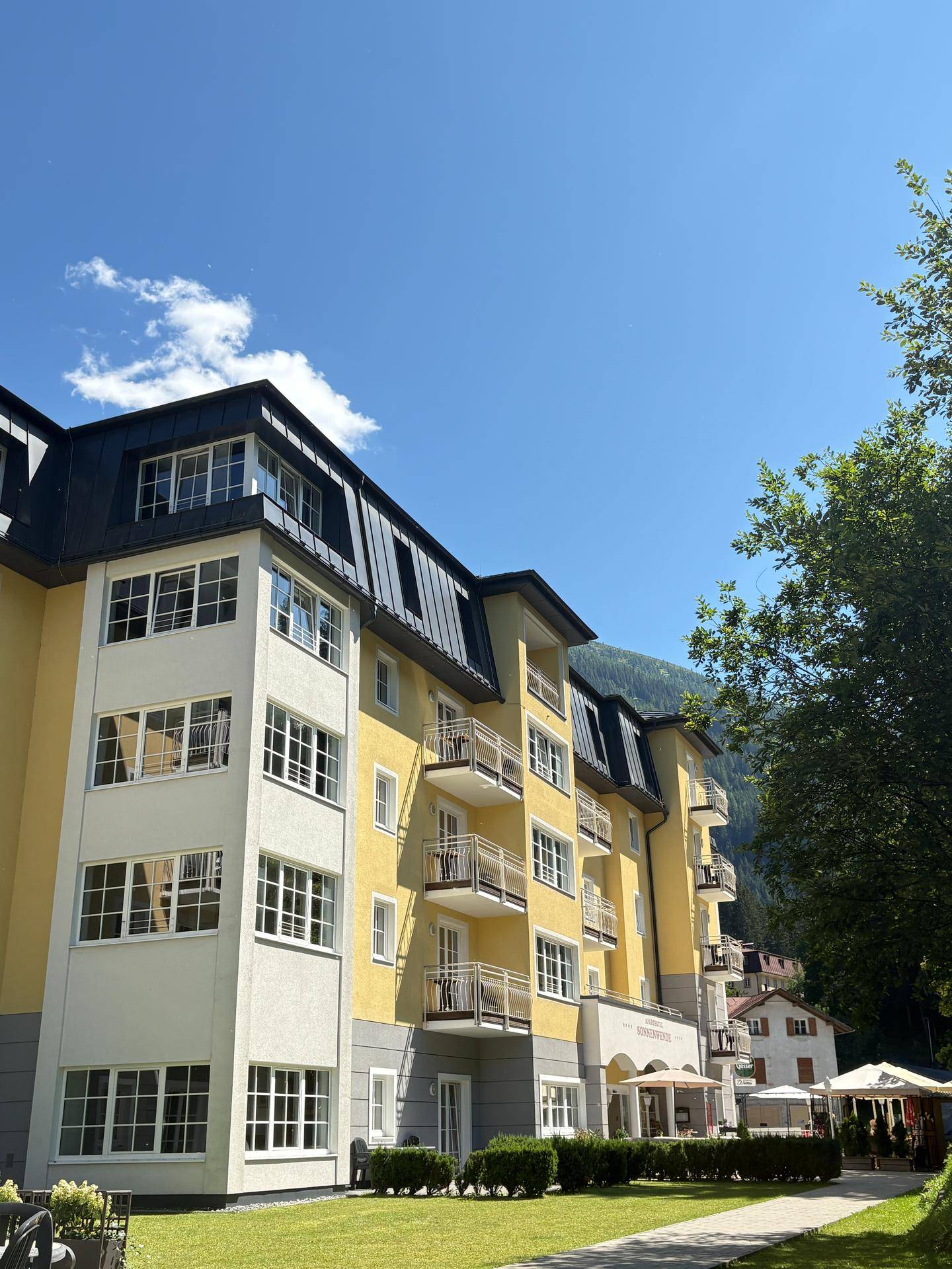 Attraktives Mehrfamilienhaus mit gelber Fassade, vielen Balkonen und Blick auf die umliegende Berglandschaft.