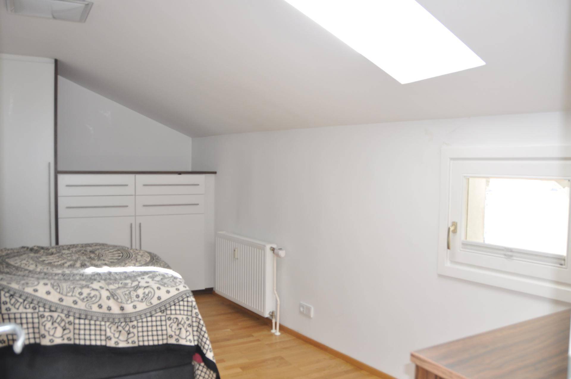 Schlafzimmer mit Dachschräge, Dachfenster und integrierten Schränken für Stauraum.
