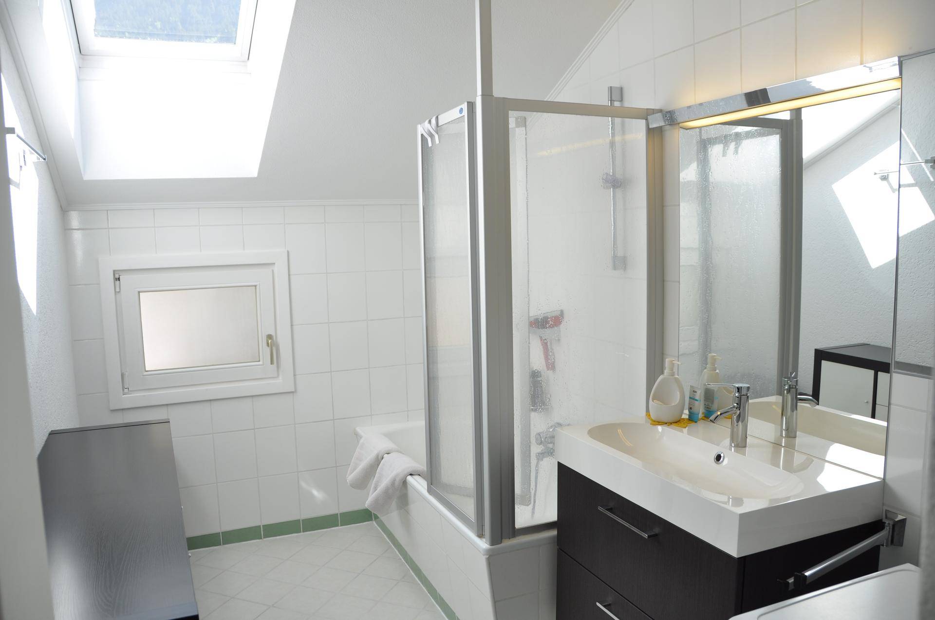Helles Badezimmer mit Badewanne, Duschabtrennung, Waschbecken und Dachfenster.