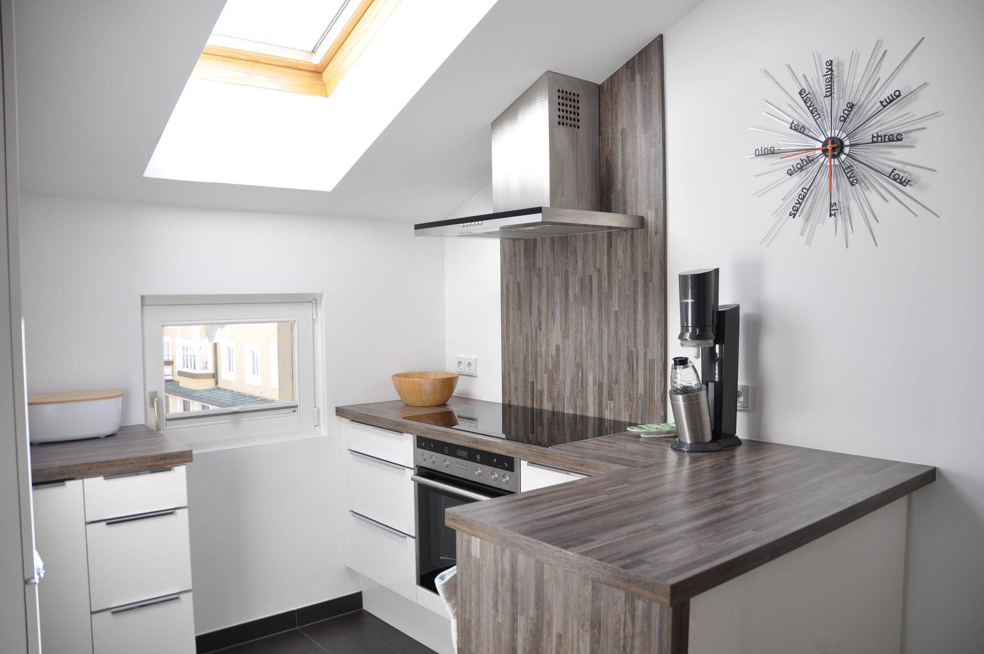 Moderne Küche mit Dachfenster, Einbaugeräten und Arbeitsplatten in Holzoptik.