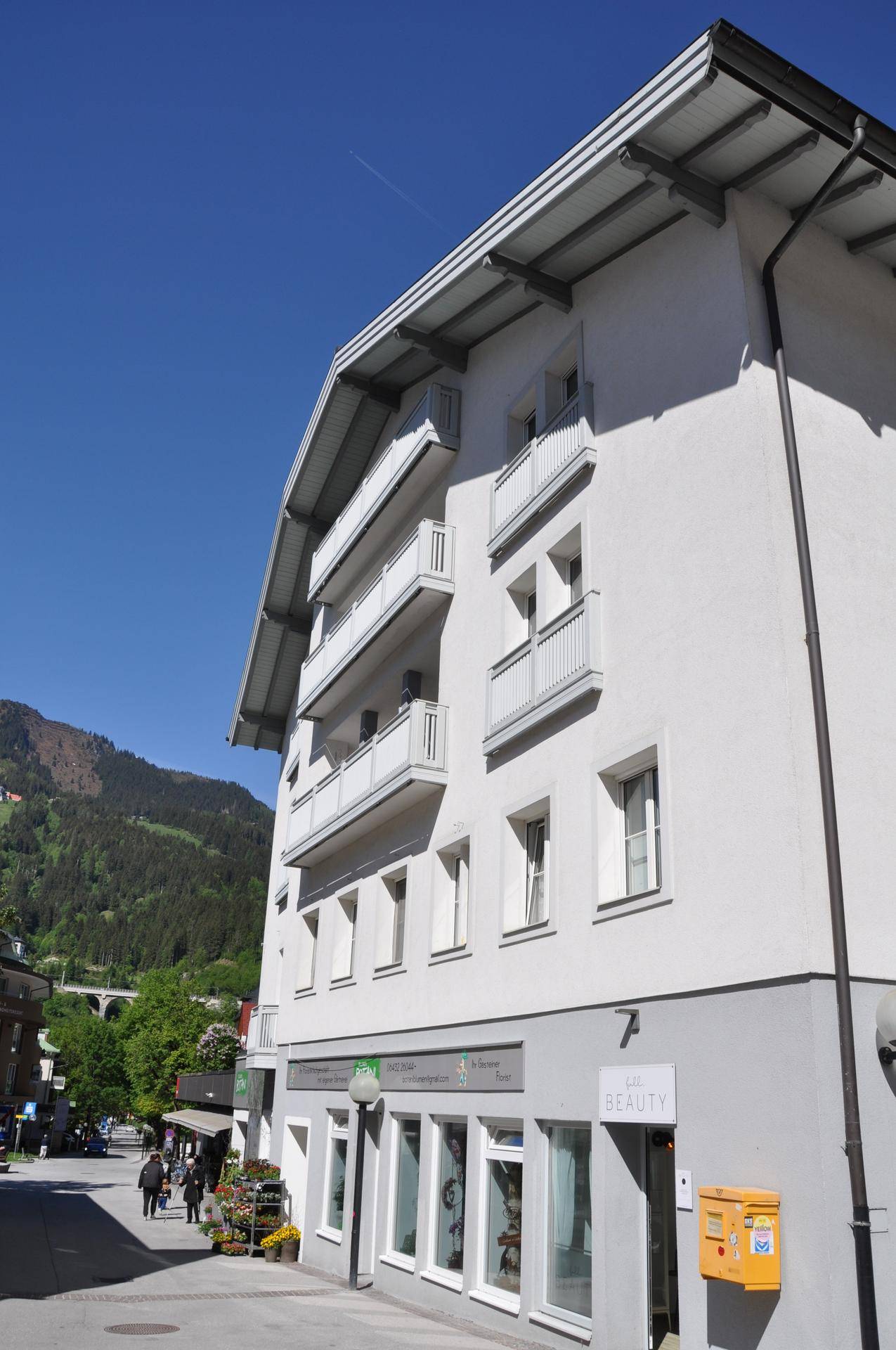 Mehrstöckiges Gebäude mit Balkonen und Geschäften im Erdgeschoss in einer städtischen Umgebung.