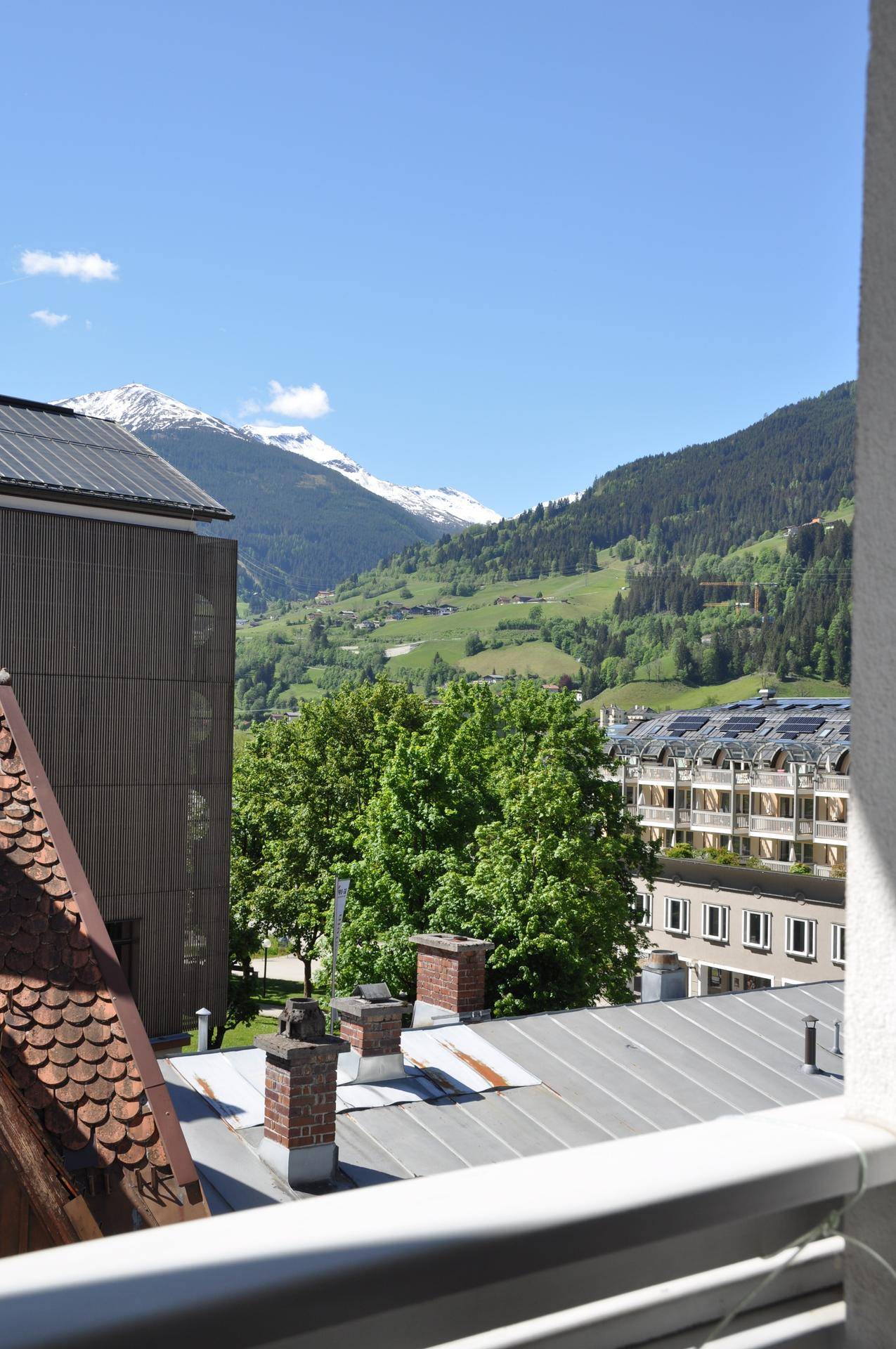Panoramablick auf schneebedeckte Berge und grüne Hügel von einem oberen Stockwerk.