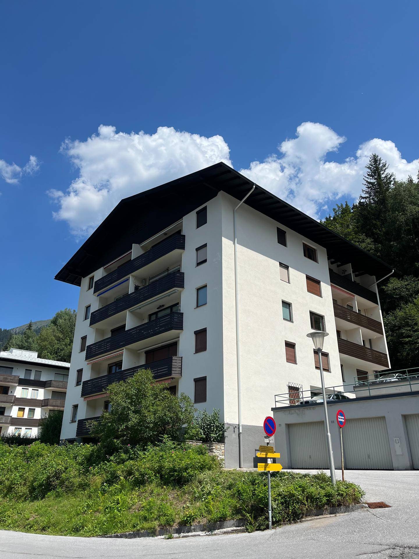 Mehrstöckiges Wohngebäude mit Balkonen und Garagen, umgeben von grüner Natur unter blauem Himmel.