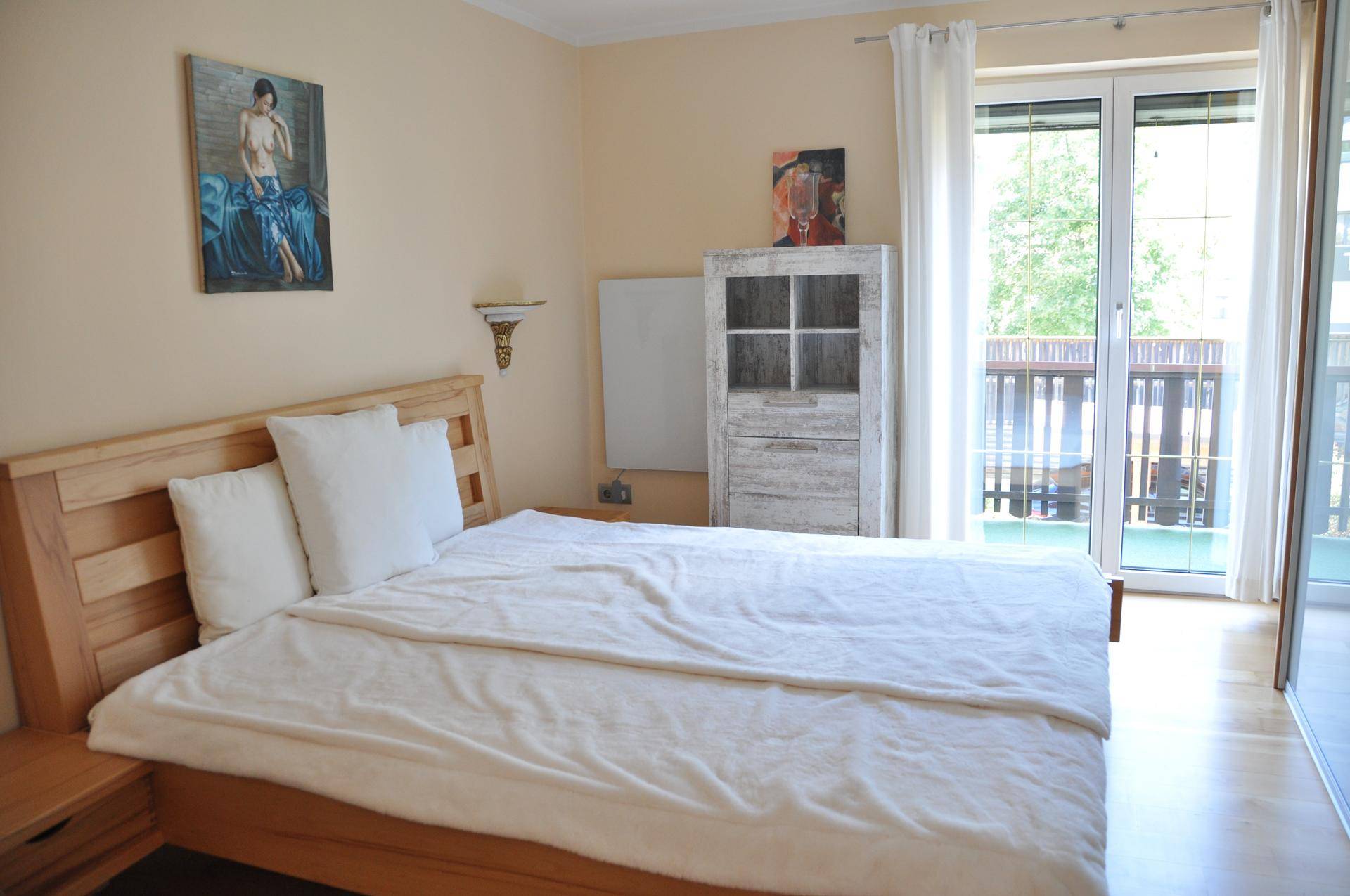 Gemütliches Schlafzimmer mit hellem Holzbett, Parkettboden und direktem Zugang zum Balkon.