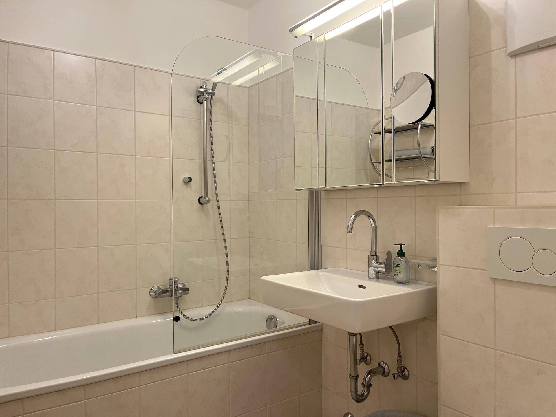 Funktionales Badezimmer mit Badewanne, integrierter Dusche, Waschbecken und hellen Fliesen.