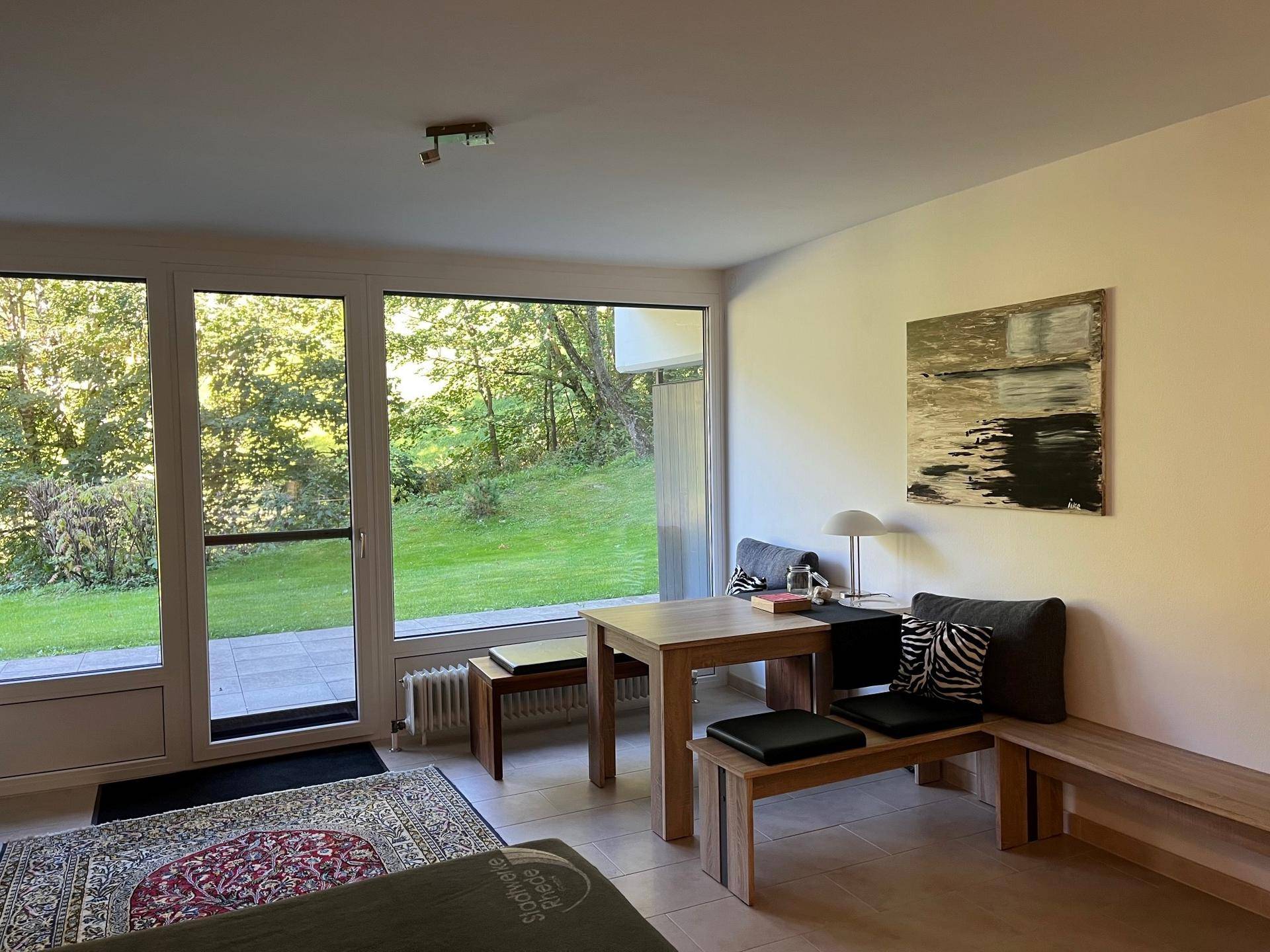 Gemütlicher Wohnbereich mit Esstisch, großen Fenstern und Blick ins Grüne sowie Terrassenzugang.