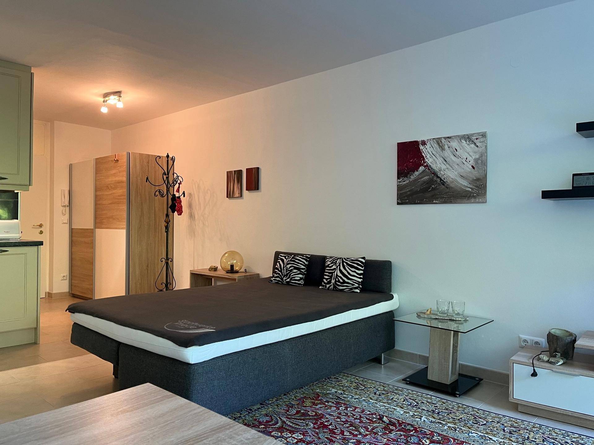 Schlafbereich mit Doppelbett, Nachttischen und einem Kleiderschrank im offenen Studio-Layout.